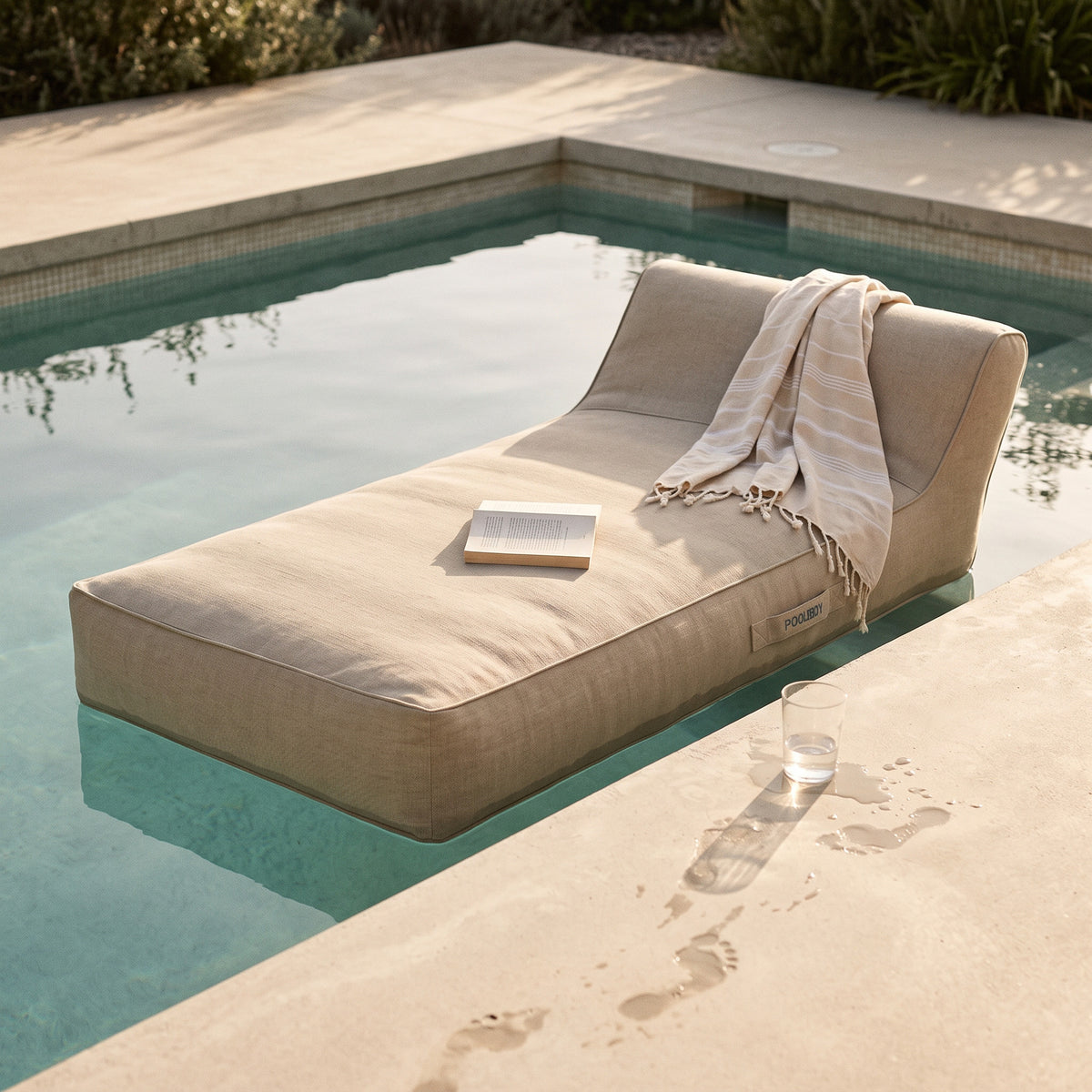 Poolboy Floata-Long in Natural beige by the pool, a towel left over it.