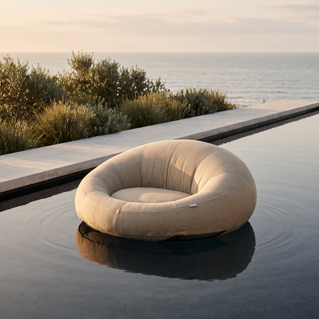 Poolboy Floata-Round in Natural floating on a coastal infinity pool at golden hour