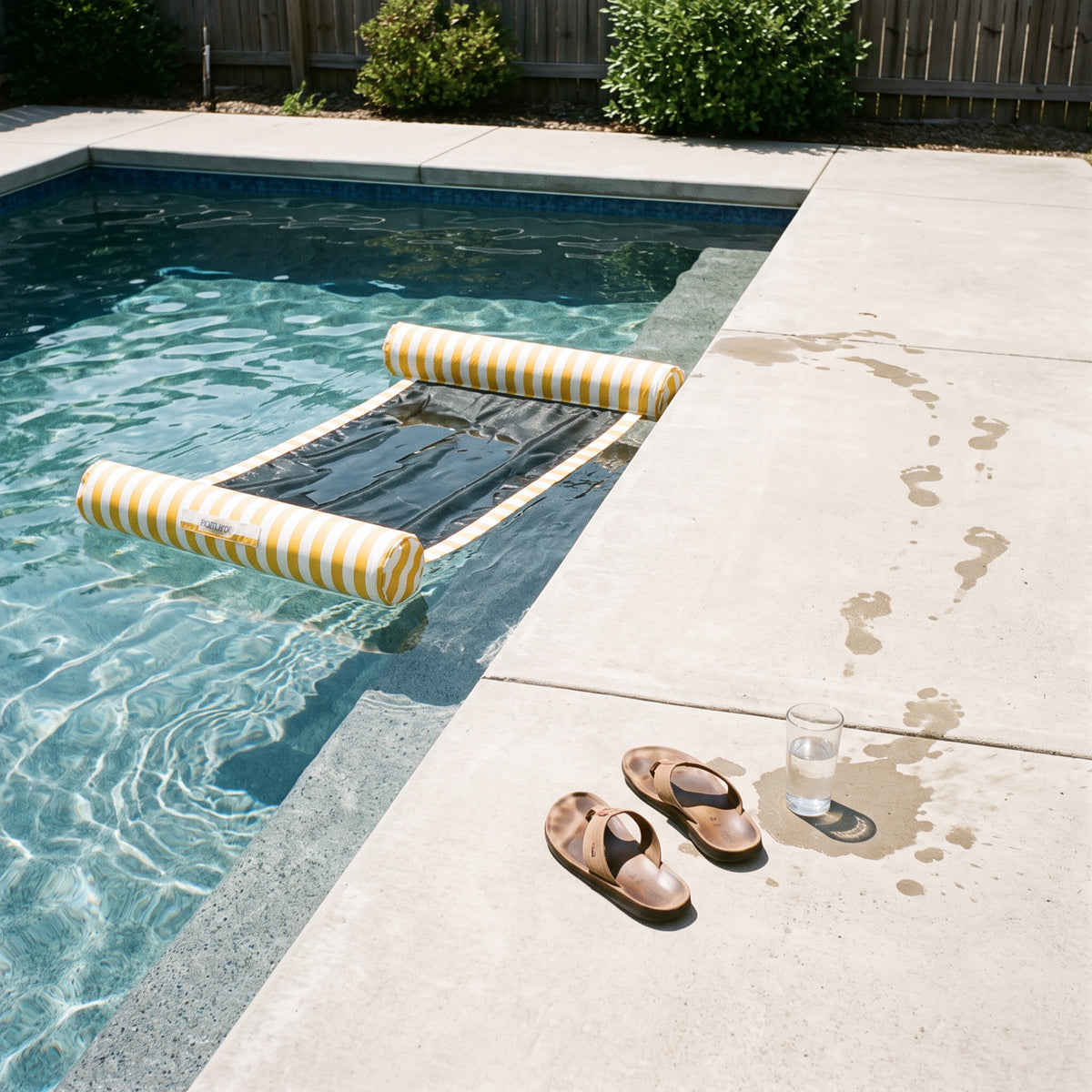 Poolboy Sinka-Bit in Yellow and White stripe in the pool, a towel left on the paving.